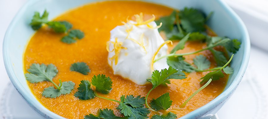 En skål med en orange soppa på en tallrik 