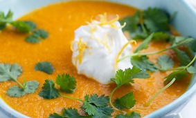 En skål med en orange soppa på en tallrik 
